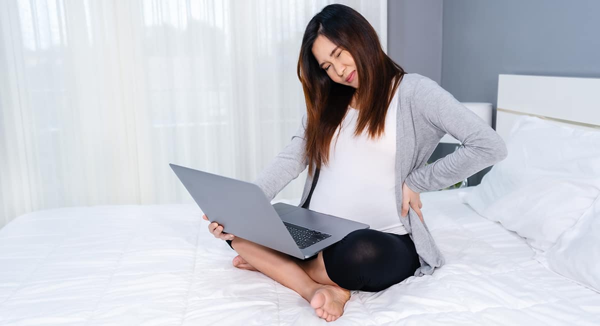Pregnant woman experiences back pain while working from home on her bed