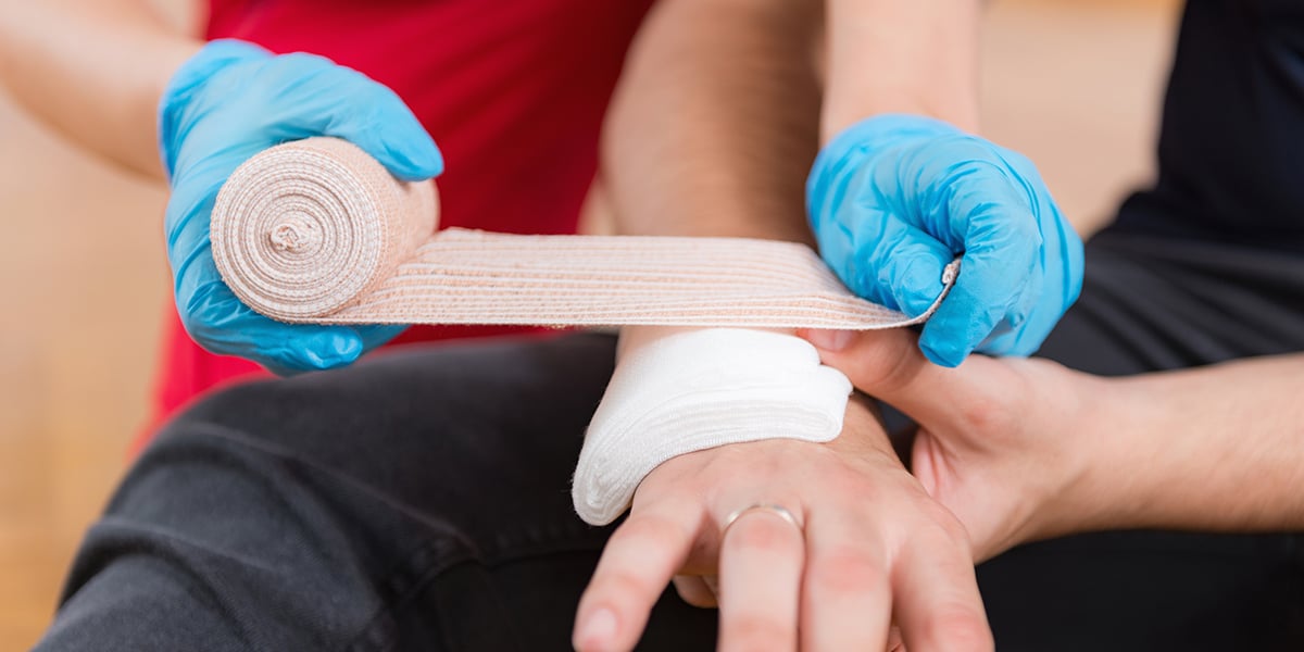 Someone applying a bandage over a dressing to hold it in place over an injury