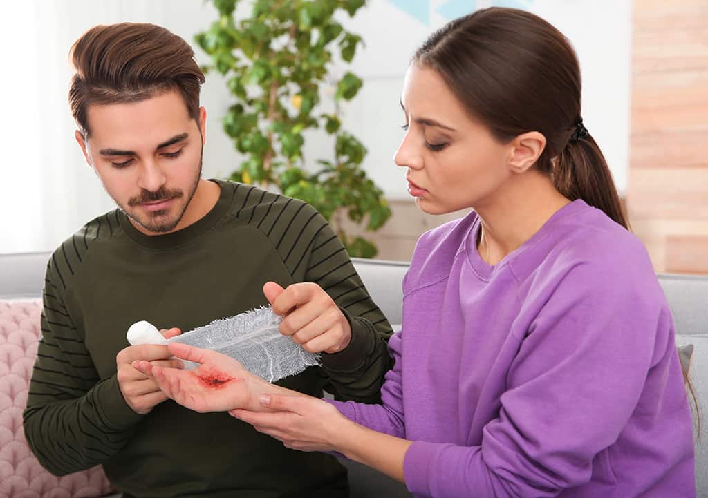 A man helps a woman to treat a minor burn injury by covering it with a bandage 