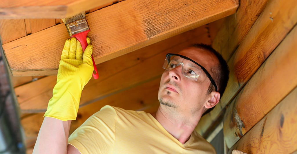 A man paints a roof interior while wearing protective goggles