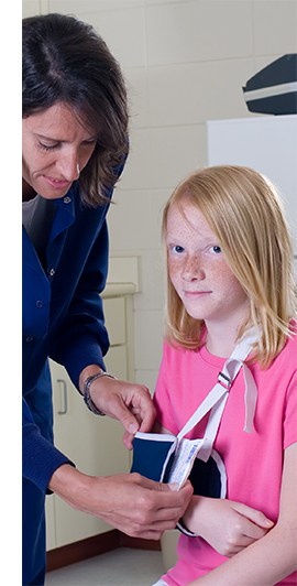 First aid trained school nurse puts a young, injured student’s arm into a sling in primary school