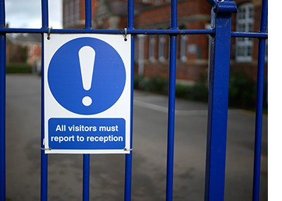 Bright blue sign on school gates helps keep children safe in school with the message “All visitors must report to reception”