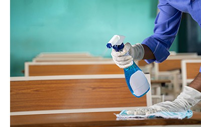 School cleaner wears vinyl gloves to protect hands from dirt and chemicals in spray while sanitising children’s desks