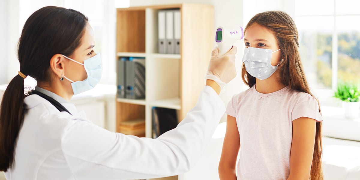 Nurse using a remote infrared thermometer to take a girl’s temperature