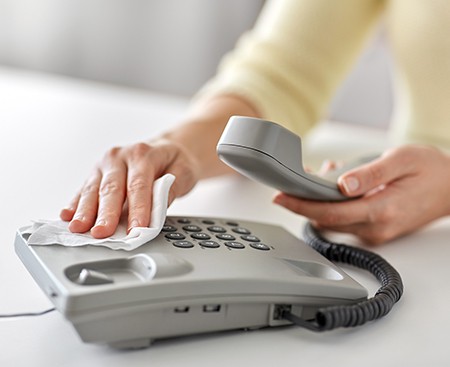 Person uses sanitising cleaning wipe to clean germs and microorganisms from an office telephone