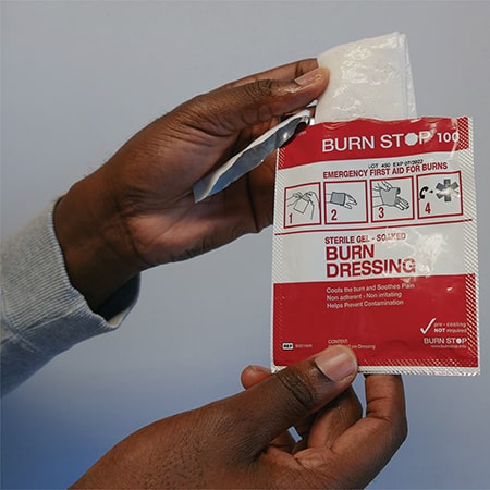 Hand takes square white Burnstop gel burn dressing out of a red and white burnstop packet
