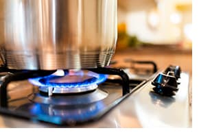 In a kitchen, large cooking pot on gas hob with flame; not dangerous but still requires safety guidance