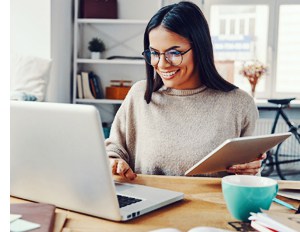 A person sits at their laptop in their home office with a first aid kit visible and accessible behind them as they work from home 