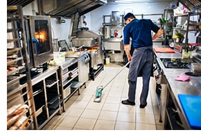 In a professional kitchen, man mops floor after a spill to improve safety and avoid slips, trips and falls
